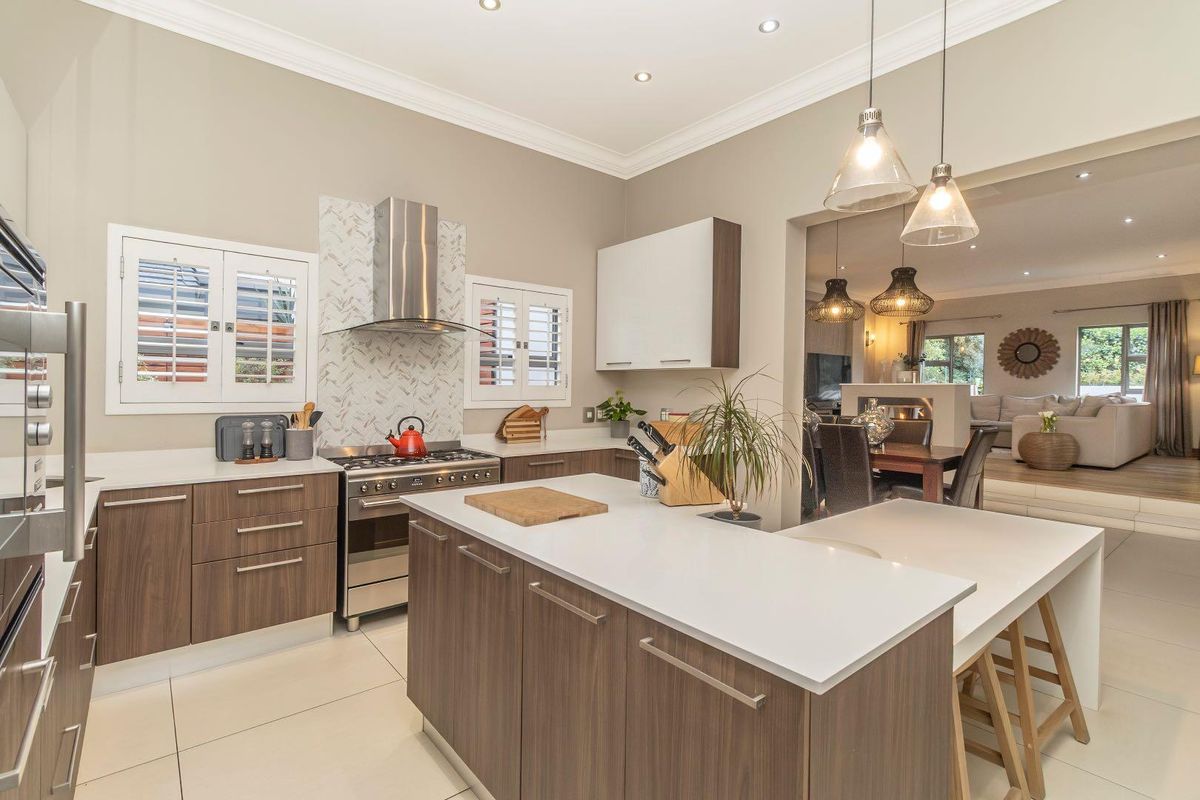 Modern kitchen featuring a central island, stone countertops, gas stove with extractor fan, and sleek cabinetry, seamlessly flowing into the adjacent dining and living areas.