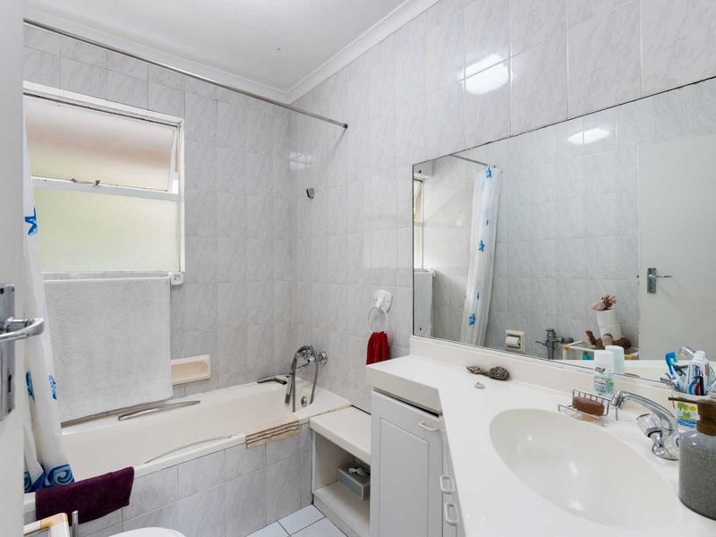 A functional bathroom featuring a built-in vanity with integrated basin, a bathtub with shower mixer, and full-height wall tiling.