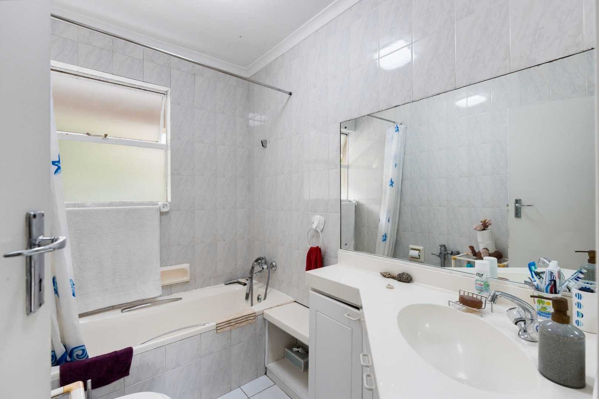 A functional bathroom featuring a built-in vanity with integrated basin, a bathtub with shower mixer, and full-height wall tiling.