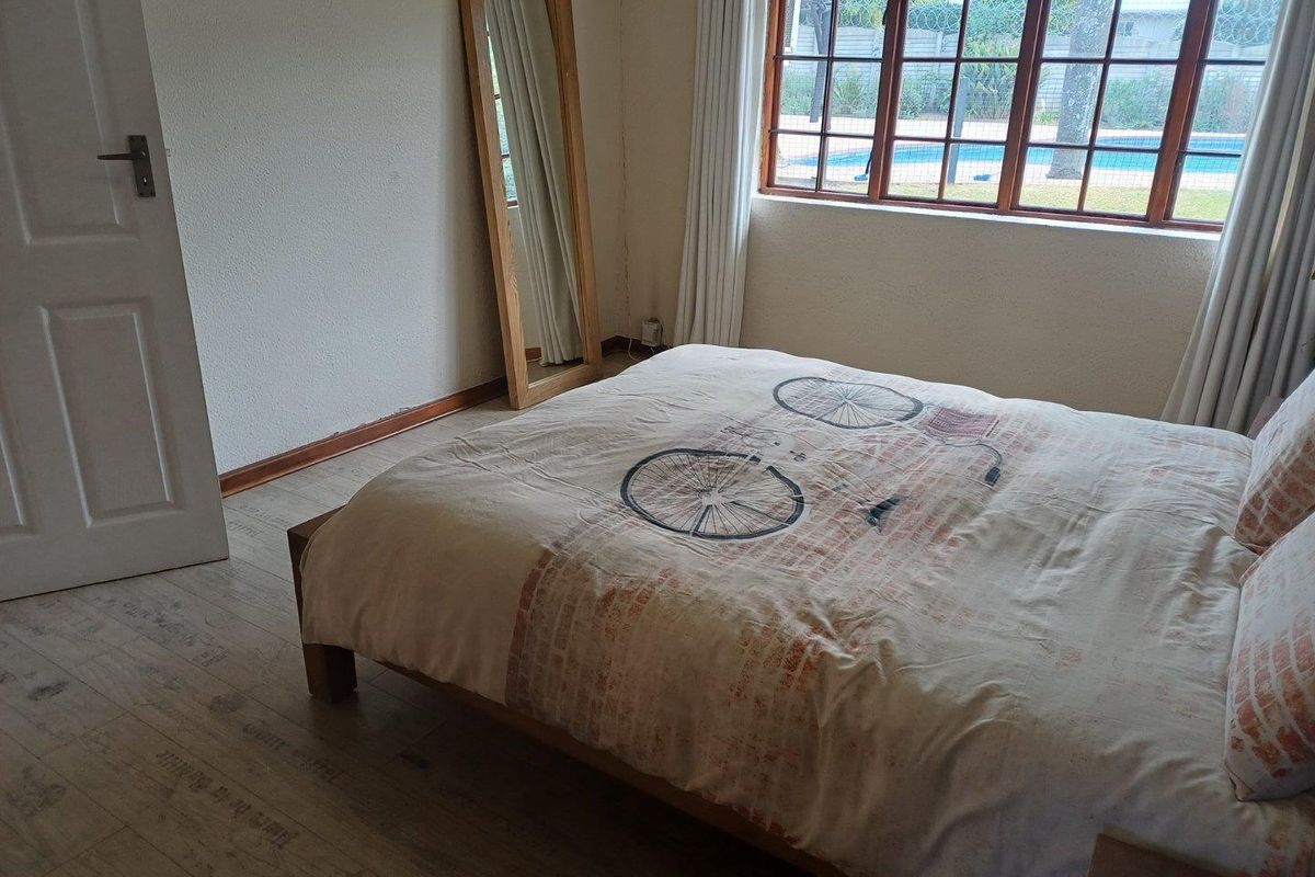 A bedroom featuring timber-look flooring and large wooden-framed windows with views of the outdoor pool area.