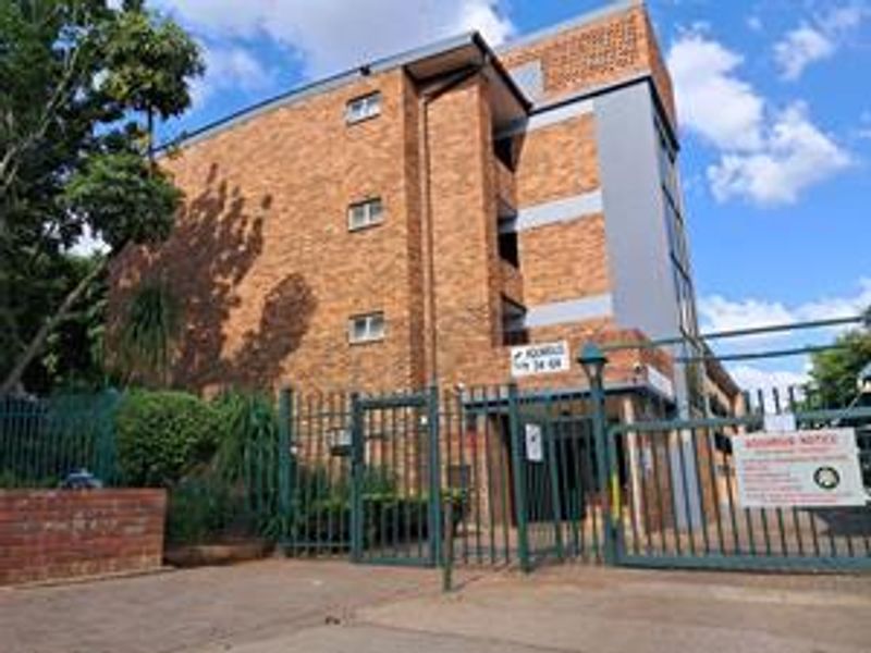 Exterior view of a multi-story brick apartment building featuring a secure gated entrance and perimeter fencing.