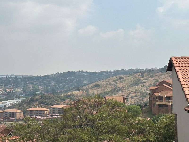 An elevated view overlooking the surrounding residential estate and hilly landscape, featuring a partial view of a tiled roof structure.