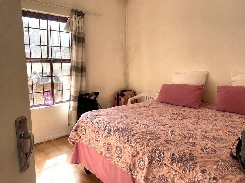 A bedroom featuring laminate flooring and a window with security bars, showing signs of wear on the walls requiring maintenance.