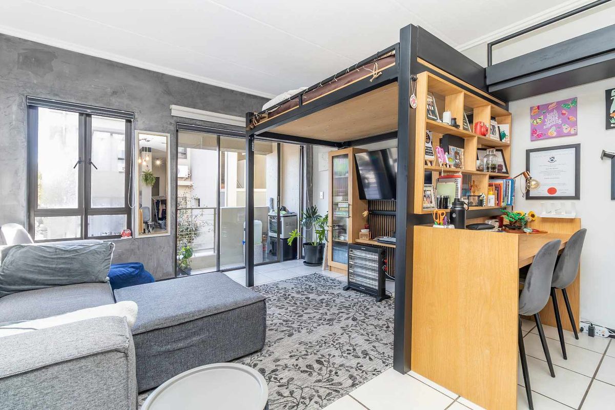 Modern open-plan apartment living area featuring a built-in loft bed structure, integrated desk, shelving, and direct access to a private balcony.