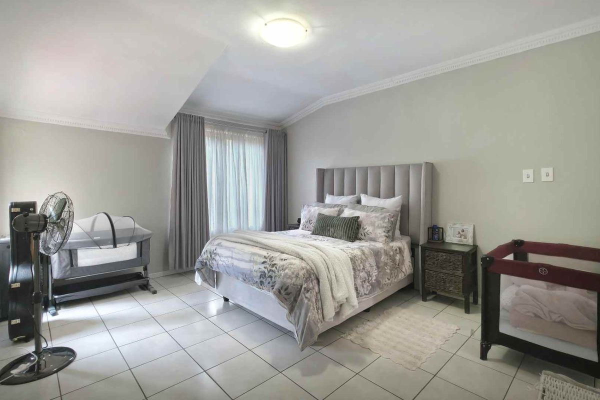 Spacious bedroom featuring tiled flooring, crown molding, and large windows with fitted curtains.