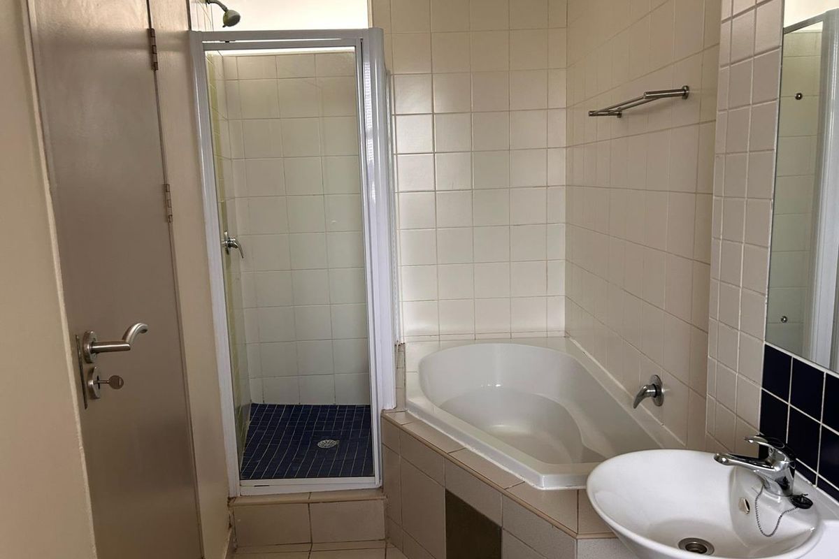A functional bathroom featuring a corner bathtub, separate shower enclosure, and a wall-mounted basin with tiled finishes.