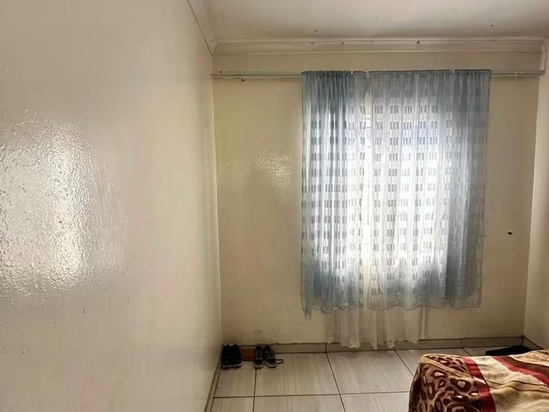 A simple bedroom featuring tiled flooring and a window with a curtain rail, requiring cosmetic updates to improve its overall condition.