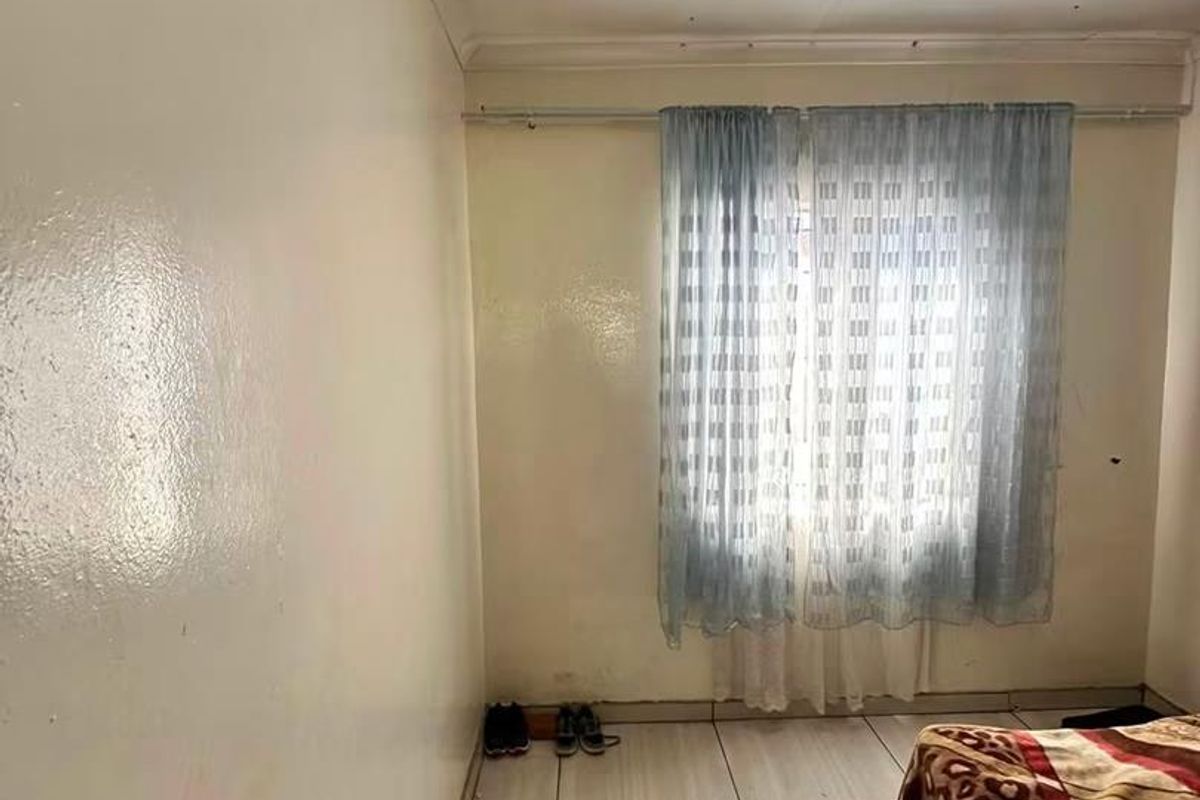 A simple bedroom featuring tiled flooring and a window with a curtain rail, requiring cosmetic updates to improve its overall condition.