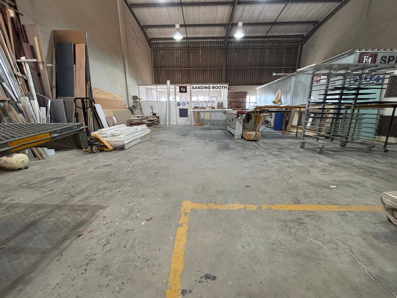 Spacious industrial workshop area featuring high ceilings with exposed steel trusses, concrete flooring, and a dedicated enclosed sanding booth.