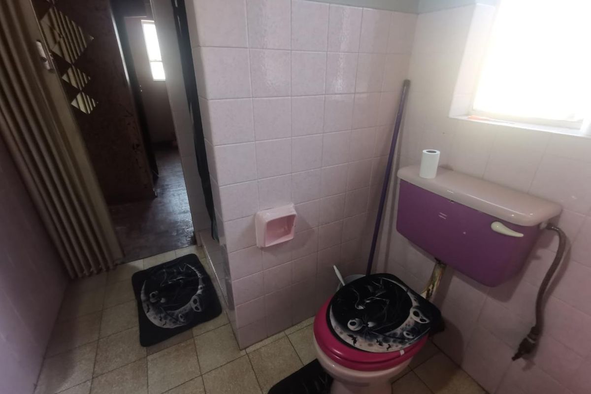 A dated bathroom featuring a vintage purple toilet cistern, tiled walls, and tiled flooring, requiring modernization to improve its aesthetic and functionality.