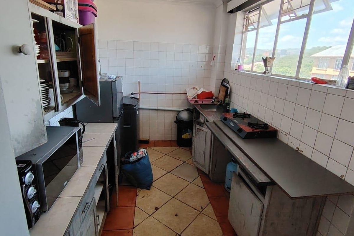 A functional kitchen featuring tiled splashbacks, built-in cabinetry, and a stainless steel sink, with large windows providing natural light and an elevated view.
