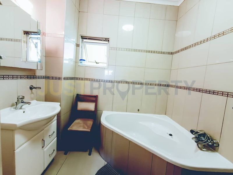 A functional bathroom featuring a corner bathtub, vanity cabinet with basin, and tiled wall finishes throughout.