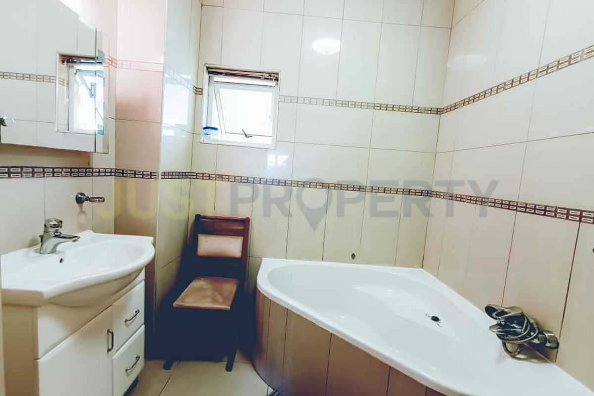 A functional bathroom featuring a corner bathtub, vanity cabinet with basin, and tiled wall finishes throughout.