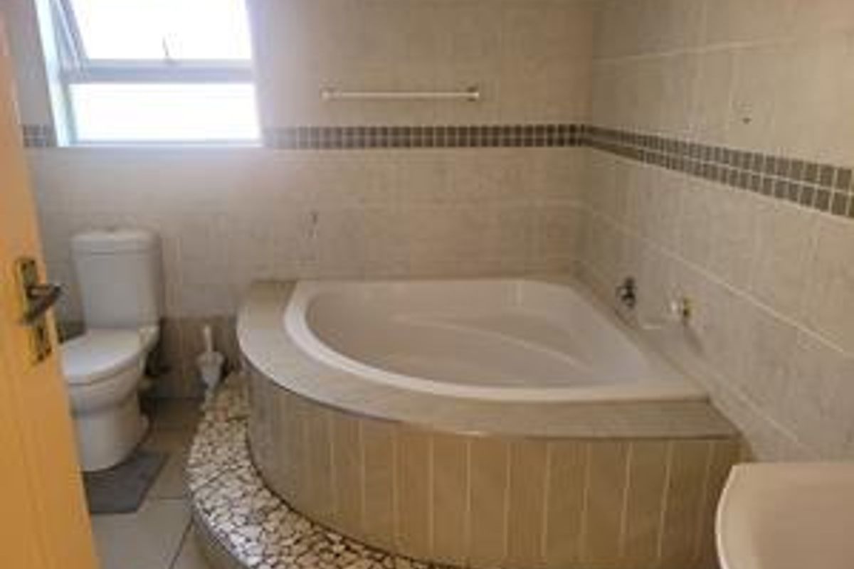 A functional bathroom featuring a corner bathtub with tiled surround, a standard toilet, and neutral wall tiling.