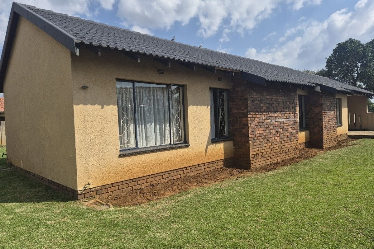Rear view of the house featuring a combination of brick and plastered exterior walls, a tiled roof, and a well-maintained lawn.