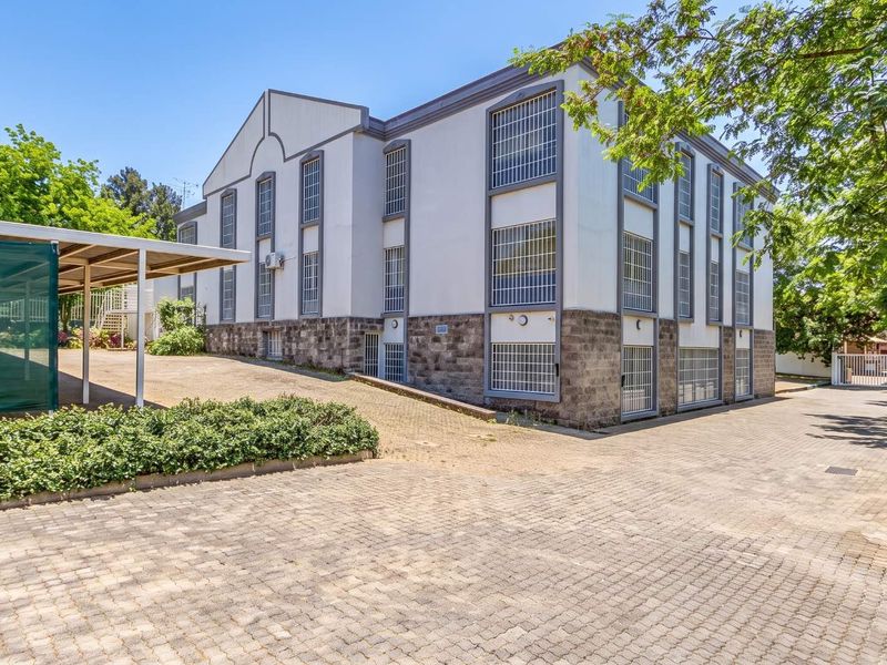 A multi-story office building featuring a stone masonry base, security-barred windows, and a paved driveway with a covered parking area.
