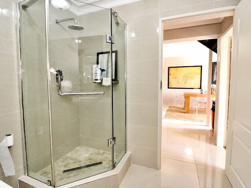 Modern bathroom featuring a glass-enclosed shower with a rain shower head and neutral wall tiling, leading into an adjacent living area.