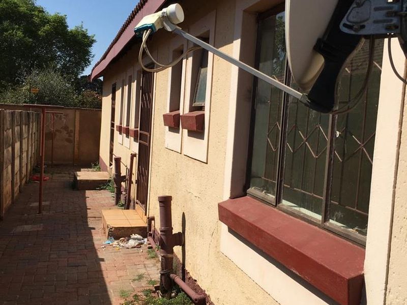 Rear exterior view of the property featuring brick paving, security gates, and a satellite dish, showing signs of wear on the exterior walls.