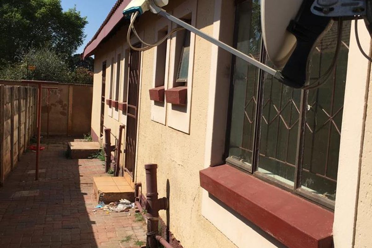 Rear exterior view of the property featuring brick paving, security gates, and a satellite dish, showing signs of wear on the exterior walls.