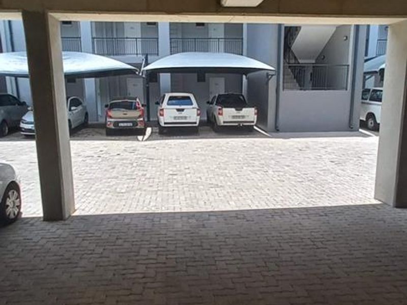 A covered parking area featuring concrete structural pillars and ceiling with paved flooring, providing sheltered vehicle storage within the apartment complex.