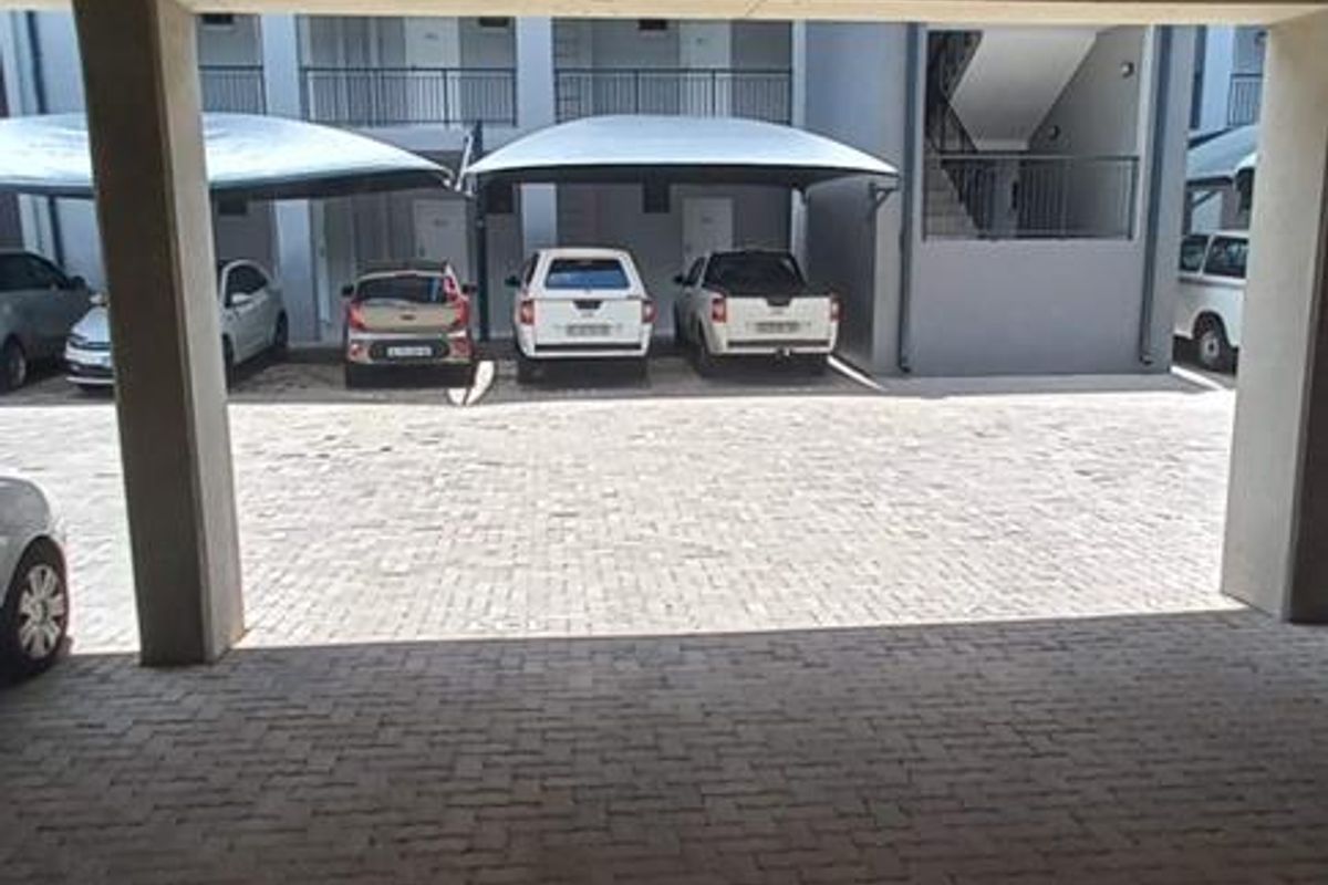 A covered parking area featuring concrete structural pillars and ceiling with paved flooring, providing sheltered vehicle storage within the apartment complex.