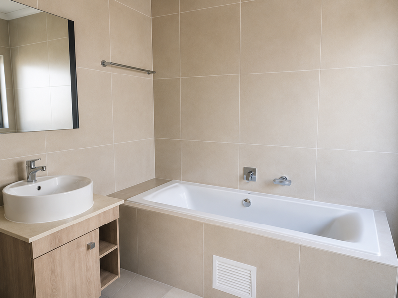 A modern bathroom featuring a built-in bathtub, a vanity cabinet with a countertop basin, and neutral wall tiling.