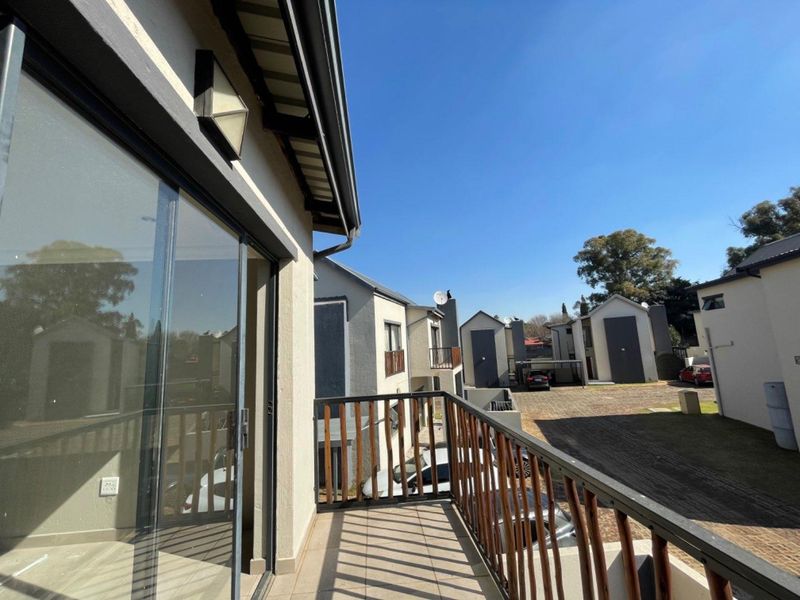 A clean, elevated balcony with tiled flooring and a wooden railing, offering views over the complex driveway and surrounding cluster units.