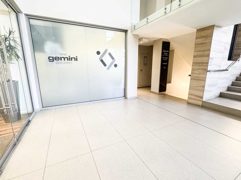 Modern commercial building entrance lobby featuring tiled flooring, glass partitions, and a staircase with a glass balustrade.