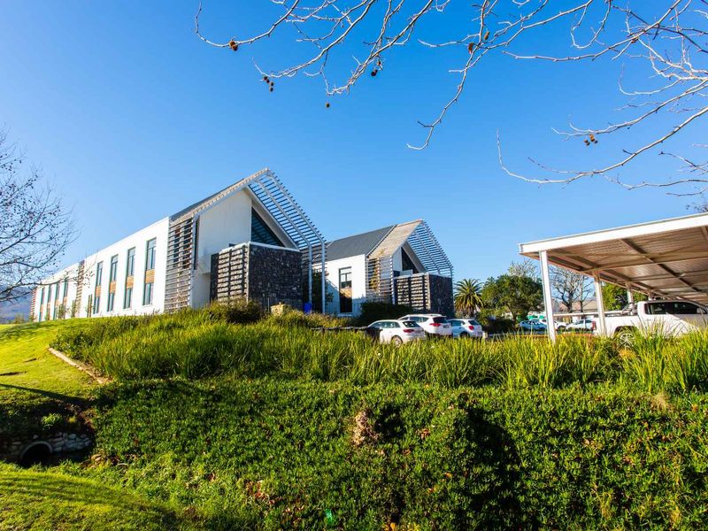 Modern office building featuring contemporary architectural design with stone cladding, metal roofing, timber louvers, and an integrated carport facility.