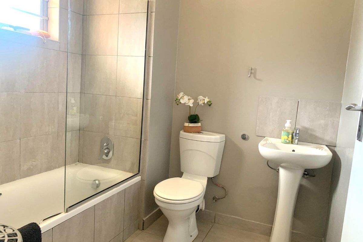 A functional bathroom featuring a bathtub with a glass shower screen, a pedestal sink, and a standard toilet with neutral wall tiling.