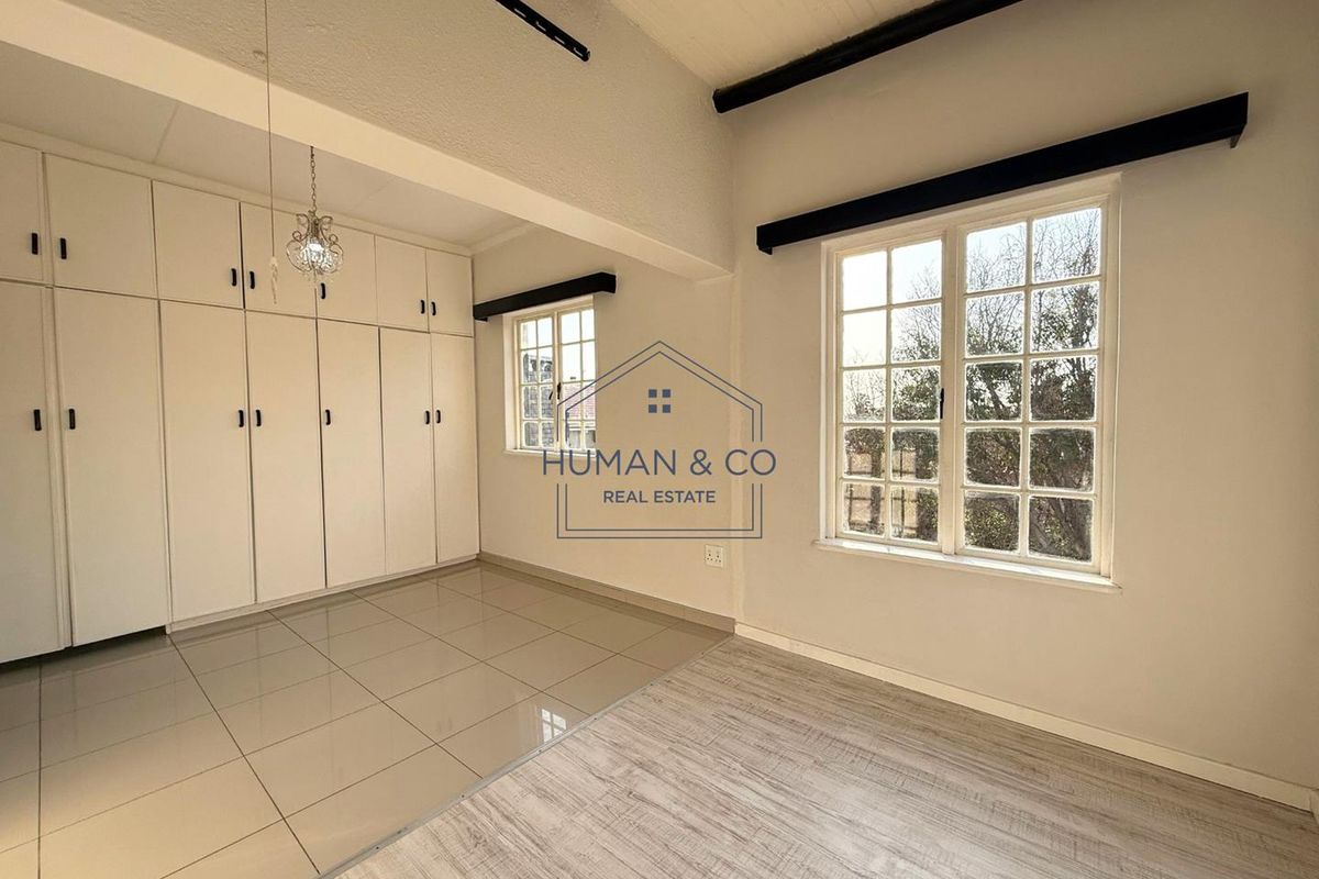 A bright bedroom featuring built-in floor-to-ceiling cabinetry, exposed ceiling beams, and large windows allowing for ample natural light.