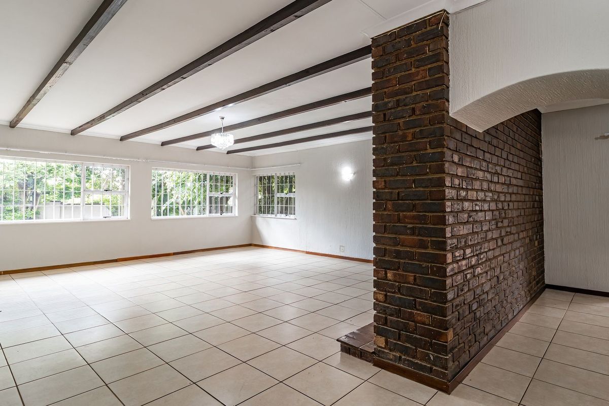Spacious living area featuring exposed timber ceiling beams, ceramic floor tiling, and a prominent exposed brick feature wall with large windows.