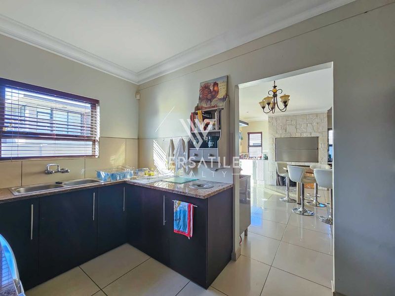 A functional kitchen featuring dark cabinetry, granite countertops, and a double sink, with an open-plan flow leading into the adjacent living area.