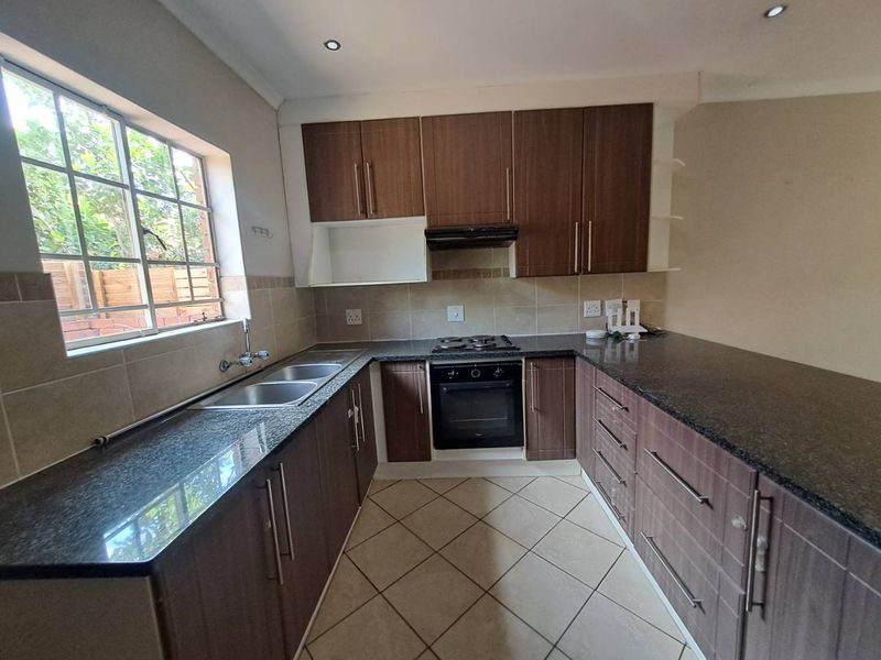 A functional kitchen featuring dark wood cabinetry, granite countertops, a built-in oven with gas hob, and tiled flooring with a double basin sink.