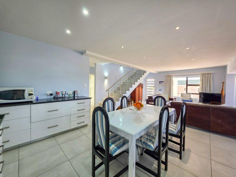Spacious open-plan living and dining area featuring modern tiled floors, recessed lighting, and a staircase with a contemporary stainless steel balustrade.