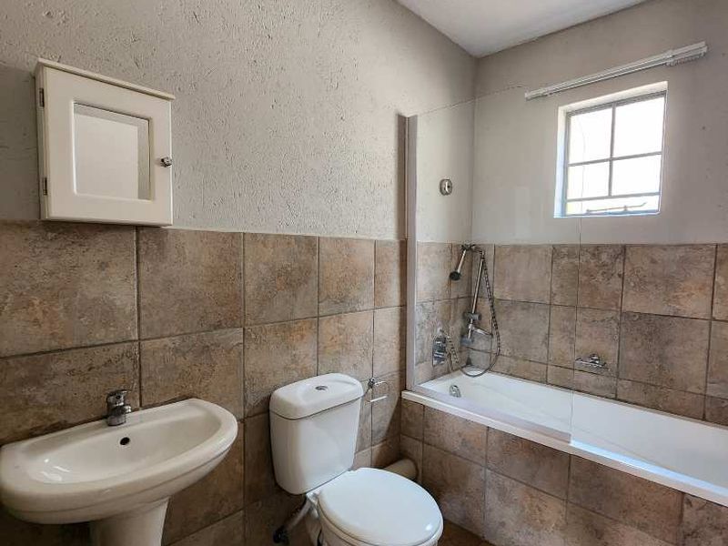 A functional bathroom featuring a pedestal basin, toilet, and a bathtub with a glass shower screen and tiled finishes.