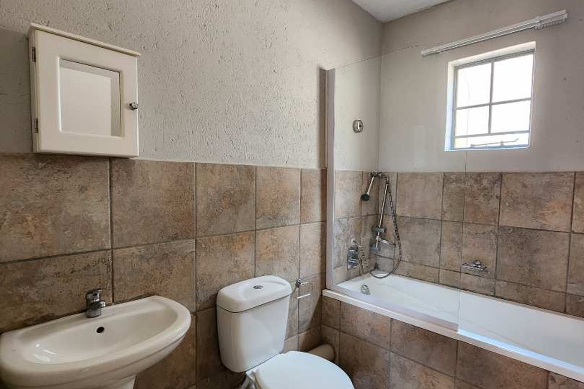 A functional bathroom featuring a pedestal basin, toilet, and a bathtub with a glass shower screen and tiled finishes.