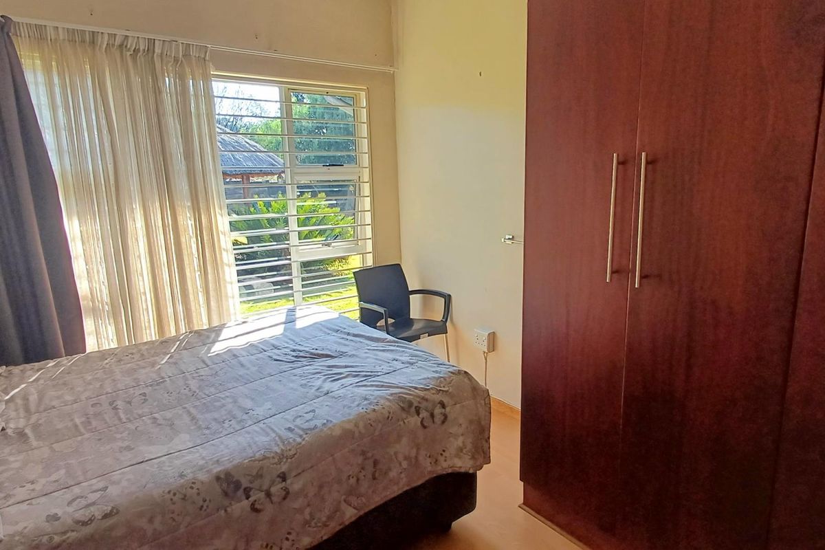A bedroom featuring a built-in wooden wardrobe and a louvered window with security bars, providing natural light and ventilation.