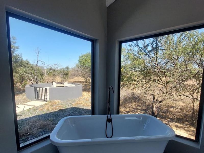 Modern bathroom featuring a sleek freestanding bathtub positioned against large corner windows with expansive views of the surrounding natural landscape.