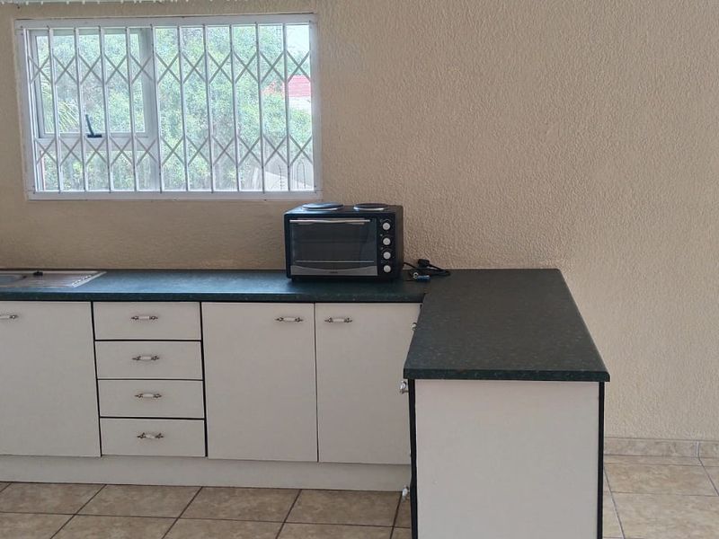 A functional kitchen area featuring white cabinetry, dark laminate countertops, a stainless steel sink, and tiled flooring, with security bars installed on the window.