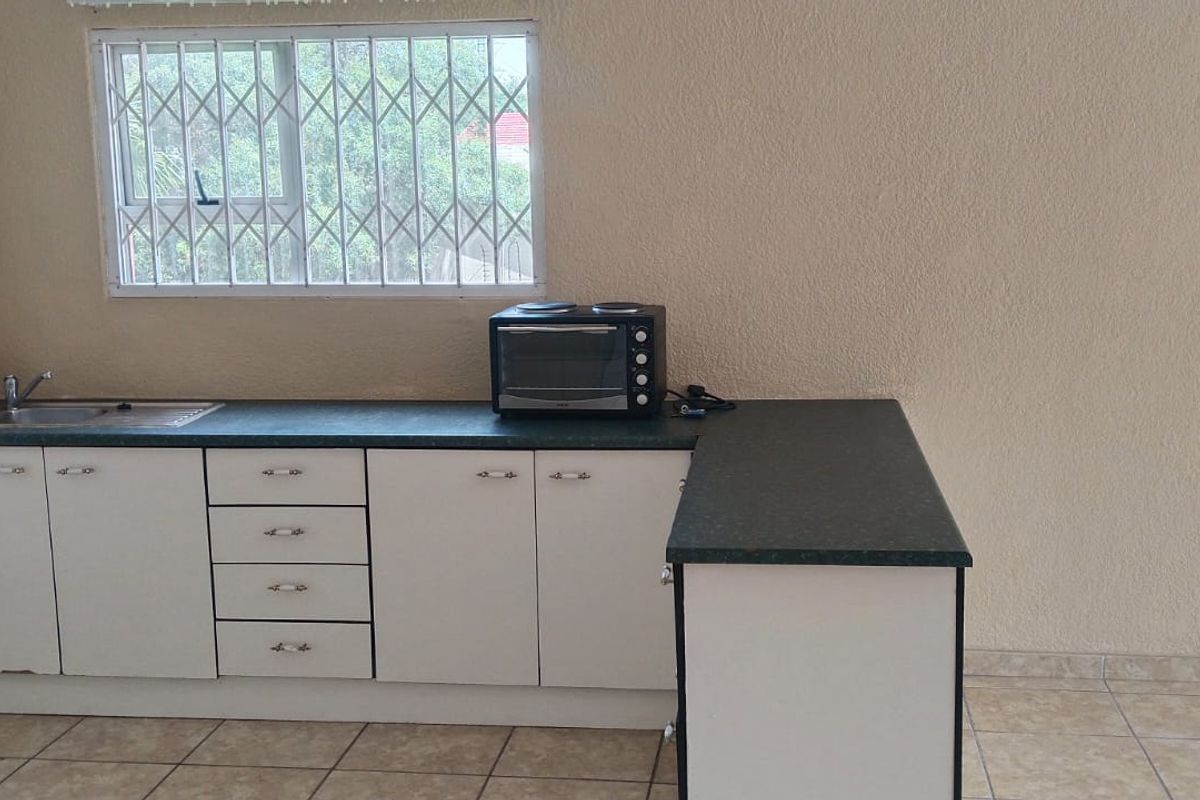 A functional kitchen area featuring white cabinetry, dark laminate countertops, a stainless steel sink, and tiled flooring, with security bars installed on the window.