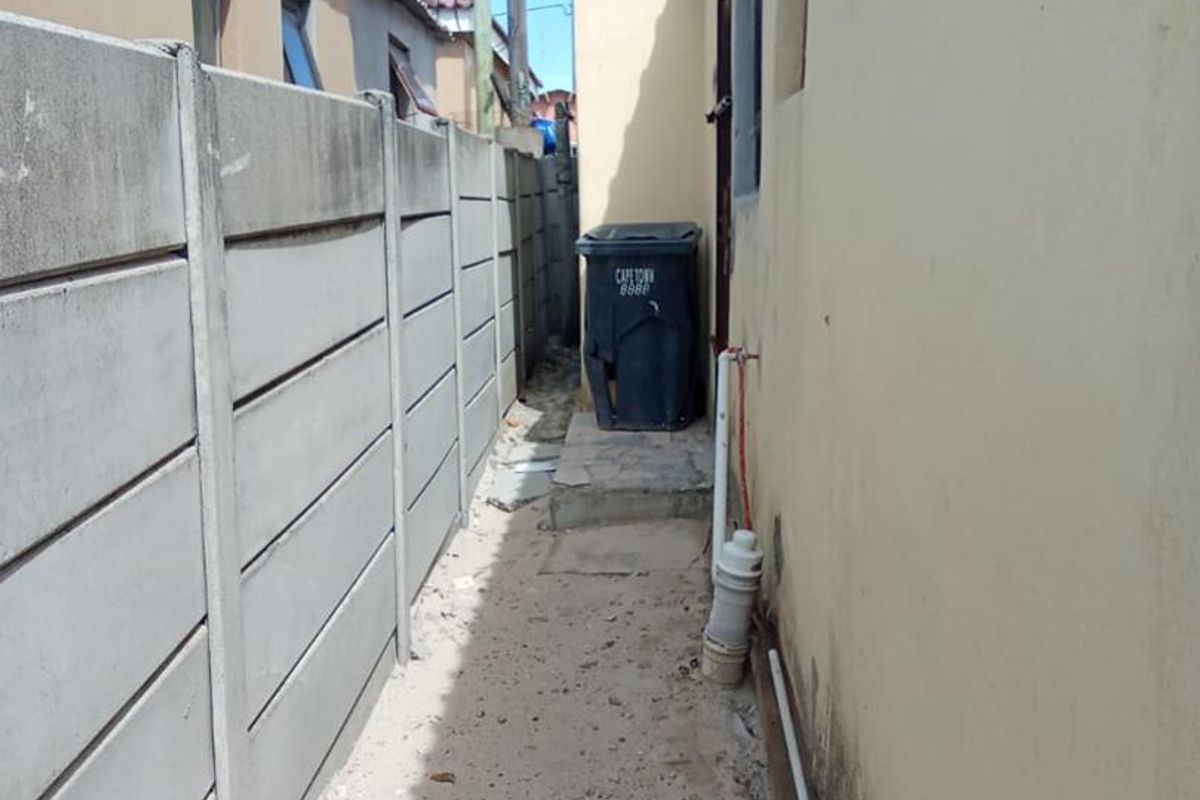 A narrow side passage of the house featuring a concrete pathway, boundary wall, and exposed exterior plumbing fixtures.