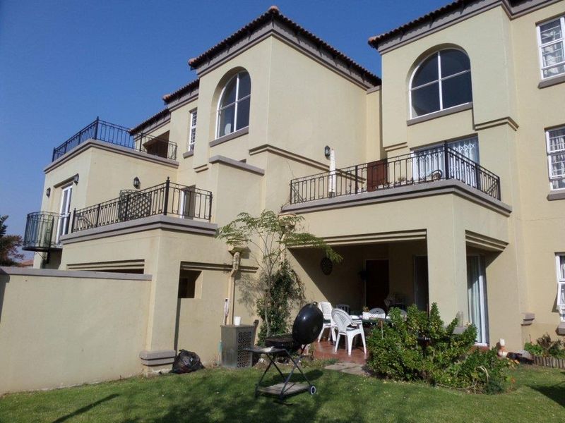 Rear view of a multi-story townhouse featuring plastered walls, arched windows, tiled roofing, and a covered patio area with balcony access.