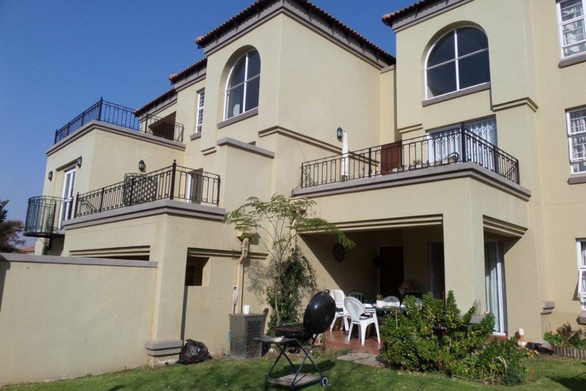 Rear view of a multi-story townhouse featuring plastered walls, arched windows, tiled roofing, and a covered patio area with balcony access.