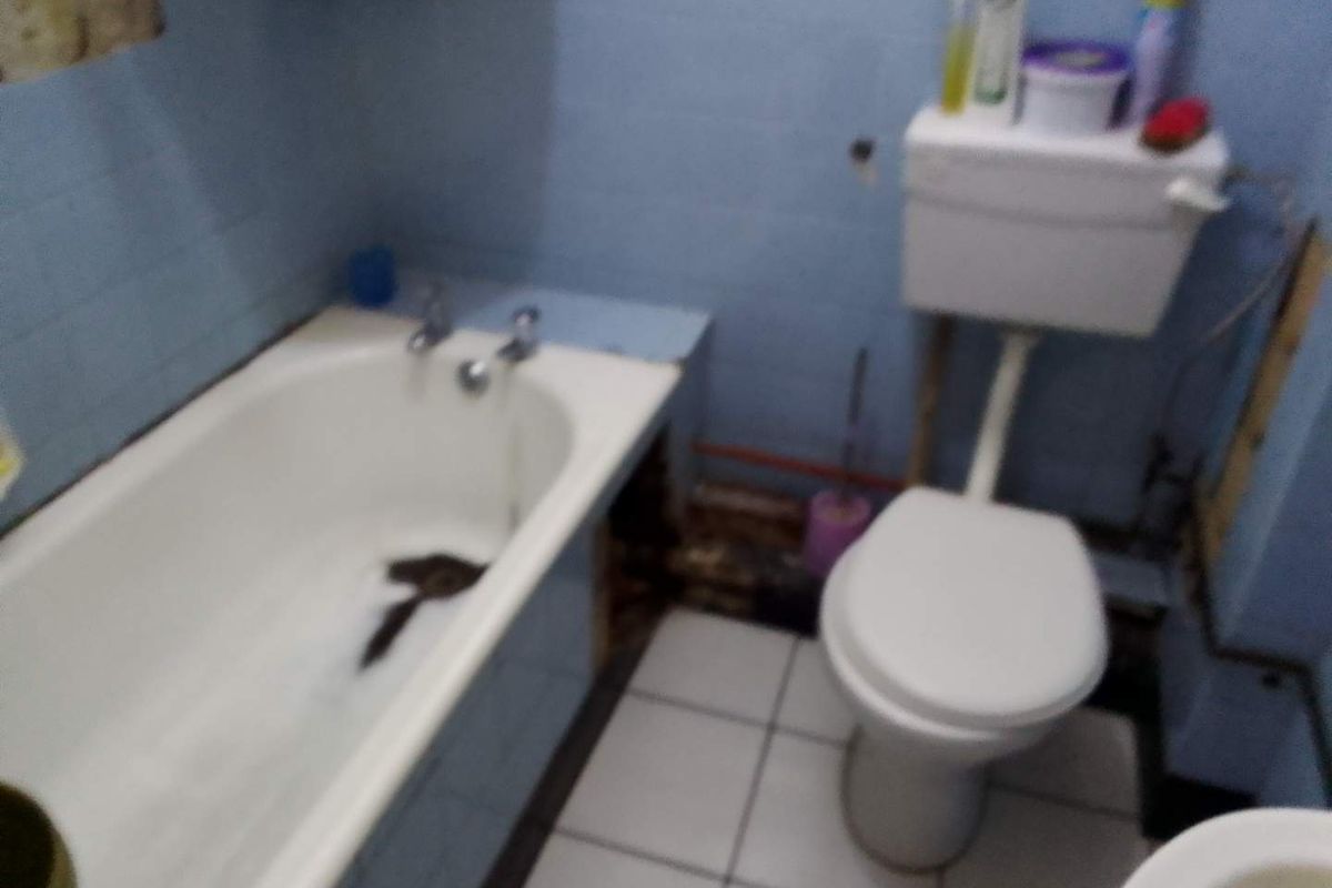 A dated bathroom featuring a bathtub and toilet with visible wall damage and exposed plumbing, requiring renovation and cosmetic updates.