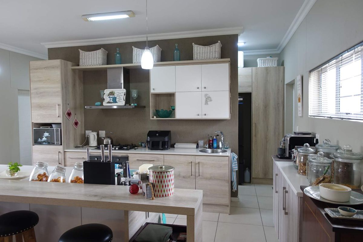 Modern open-plan kitchen featuring light wood-grain cabinetry, stone countertops, a built-in gas hob, extractor fan, and a functional breakfast bar island.