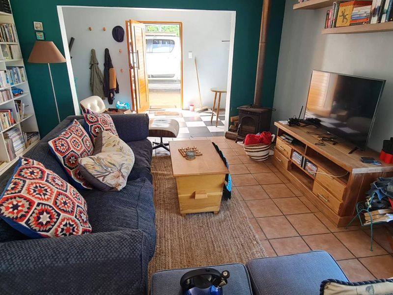 A cozy living room featuring built-in shelving, a wood-burning stove, and tiled flooring, with an open transition to an adjacent entry area.