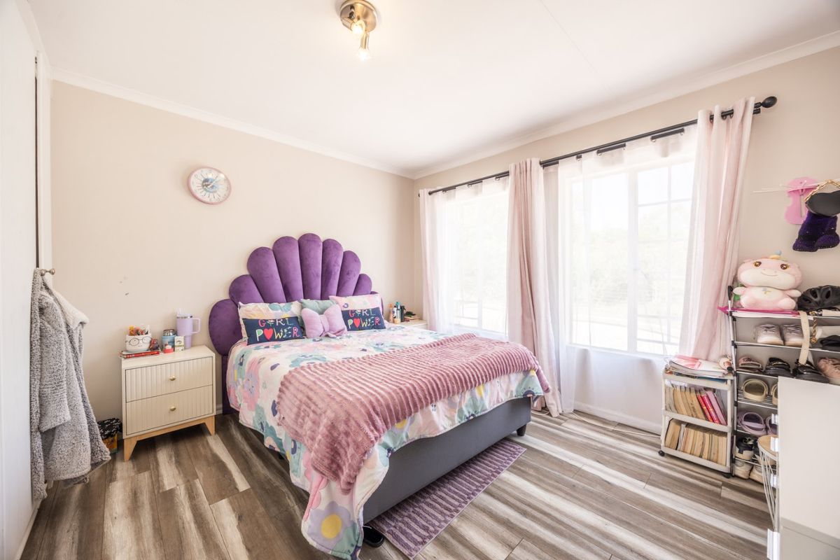 A bright and well-maintained bedroom featuring modern laminate flooring, neutral wall tones, and large windows that provide ample natural light.