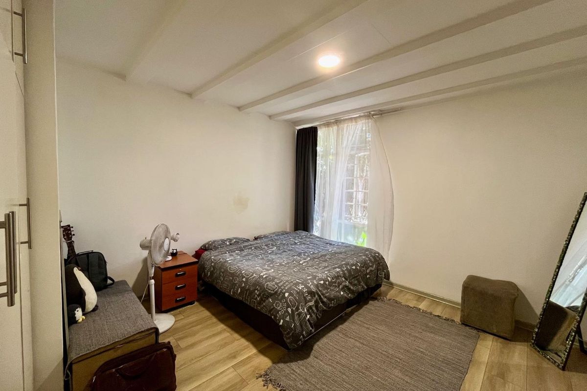 A bedroom featuring wood-look flooring, built-in cabinetry, and a window with curtains, providing a functional living space.