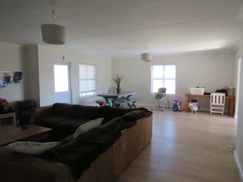 Spacious open-plan living and dining area featuring light laminate flooring, neutral walls, and ample natural light through multiple windows.